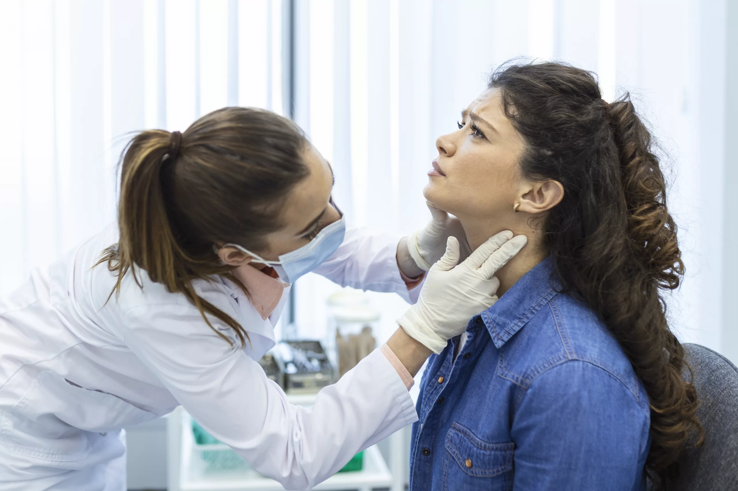 Image of an Endocrinologist examining throat of a young woman in clinic.